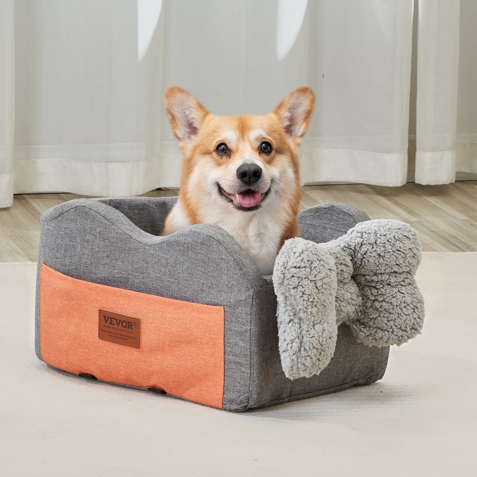 Dog sitting in a gray and orange pet bed with a fluffy blanket on a wooden floor.
